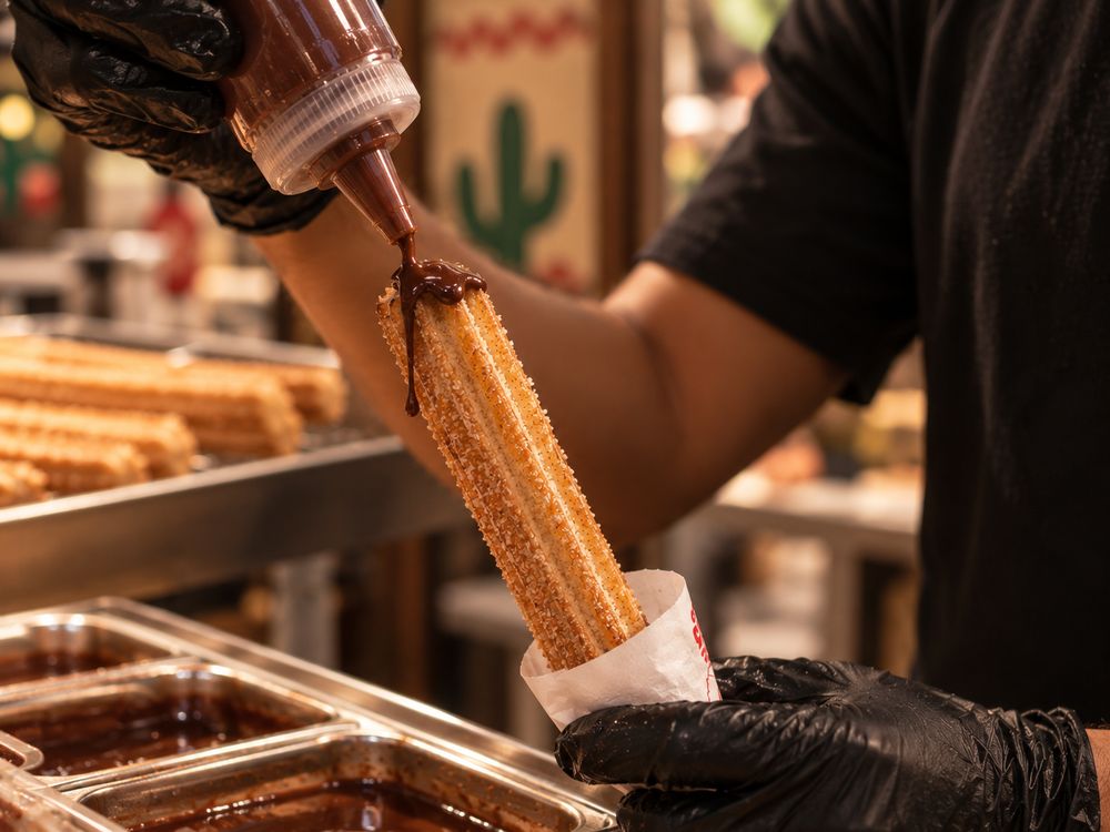 Chocolate sauce being squeezed onto a fresh churro at a churro station