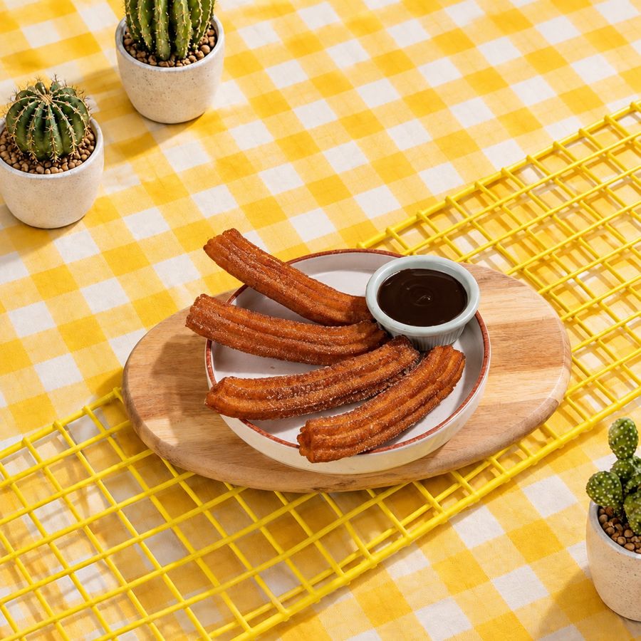 Four churros on a plate with a pot of chocolate dip