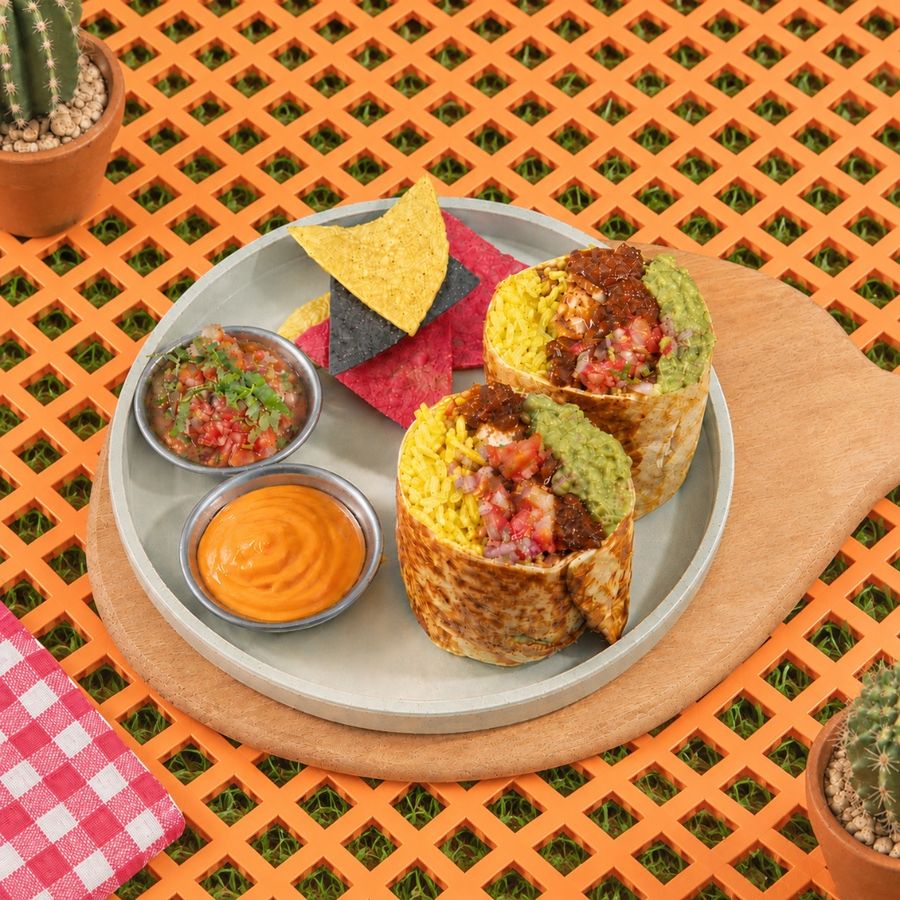 A classic burrito cut in two, with tortilla chips, salsa and an orange dip
