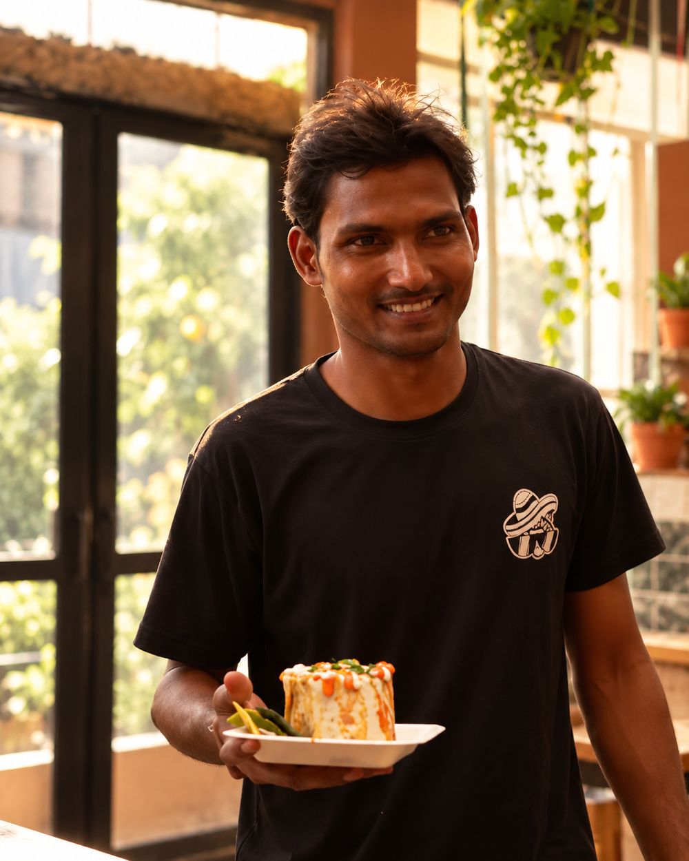 A Gracias Granny team member in a black GG T-shirt, smiling and holding a plate of food in the cafe