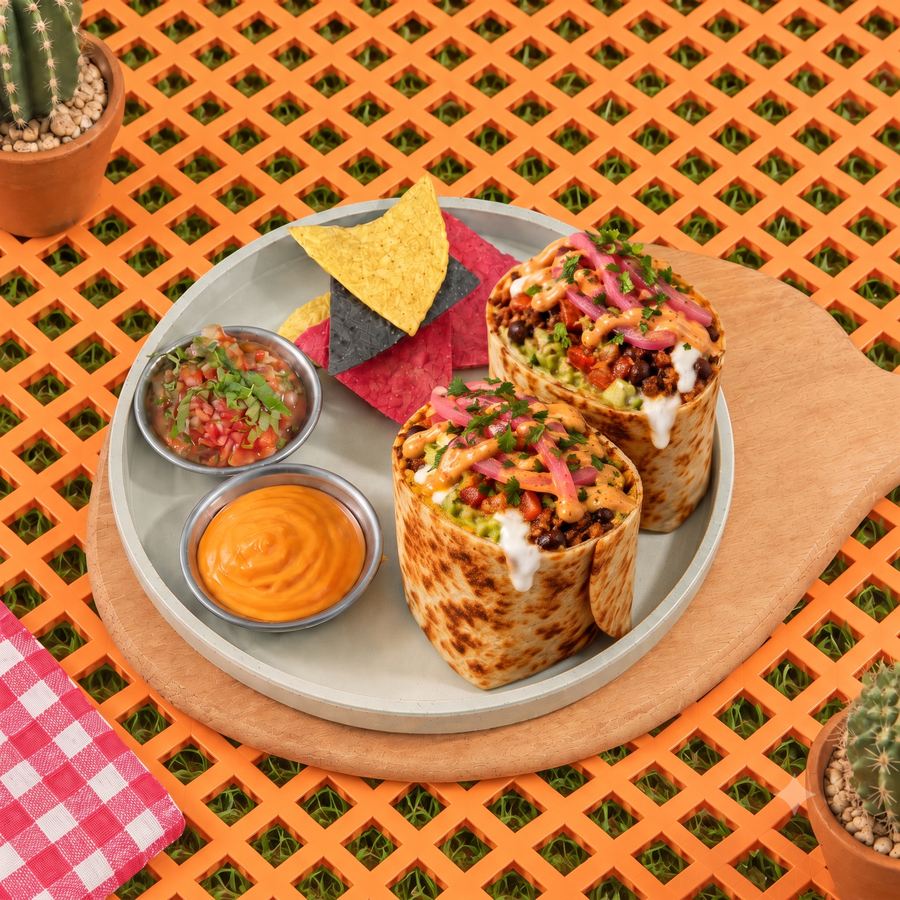 A classic burrito cut in two, with tortilla chips, salsa and an orange dip