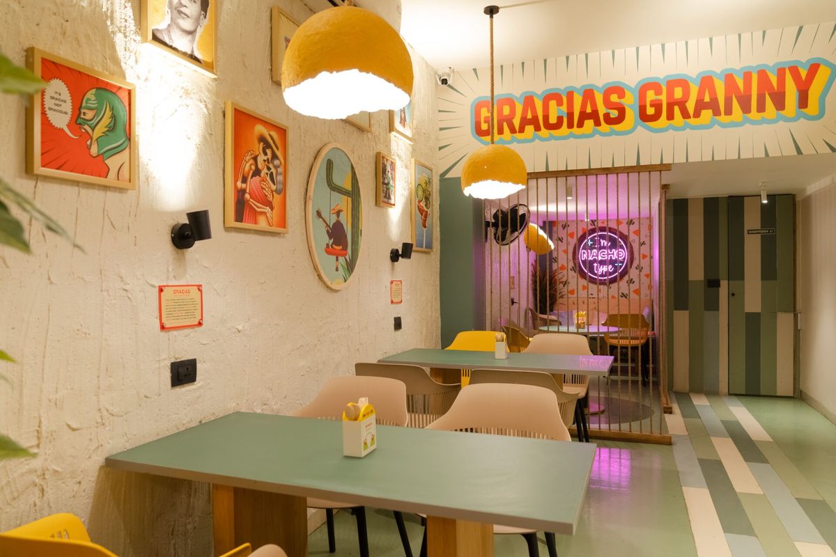 Inside GG CBD Belapur: green tables under yellow pendant lamps, framed Mexican art on the wall and the Gracias Granny sign over the doorway